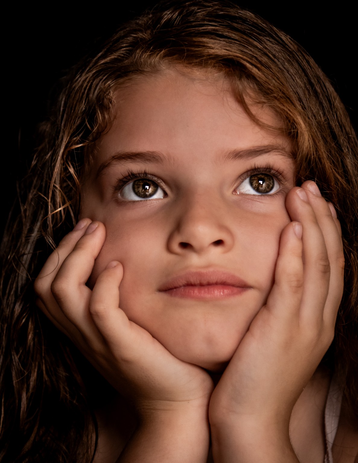 Warm fine art kinderportret van een meisje met haar handen langs haar gezicht